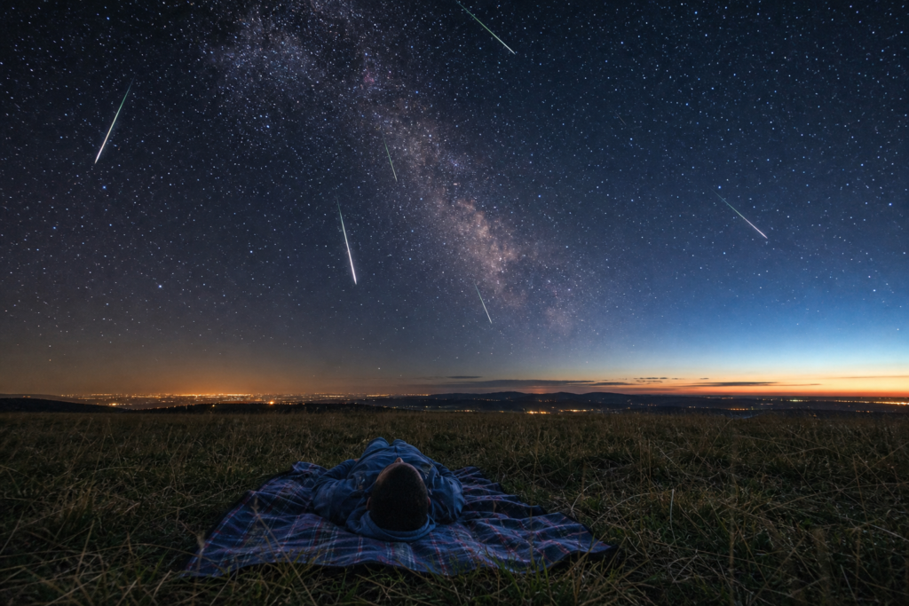 Bright meteor streaks crossing a star-filled night sky above a dark rural landscape during the Eta Aquarid meteor shower peak